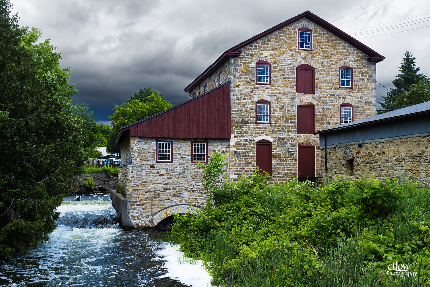 The Old Stone Mill on a clear autumn day, stone walls and red trim reflected in the millstream below