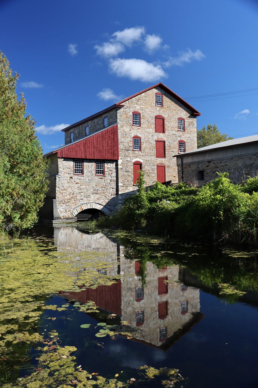 The Old Stone Mill on a clear autumn day, stone walls and red trim reflected in the millstream below