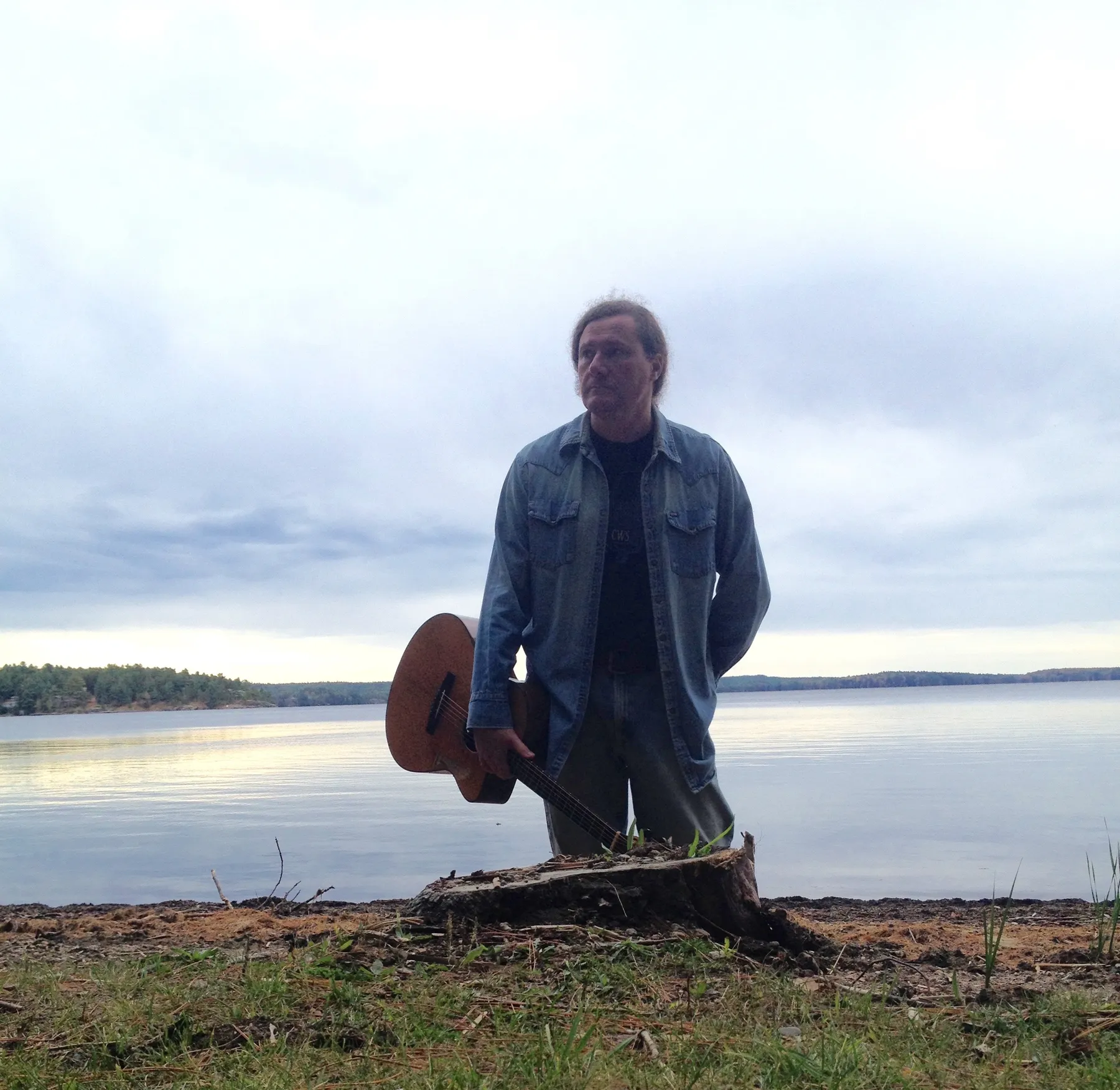 Pat Johnson standing by the water with his acoustic guitar